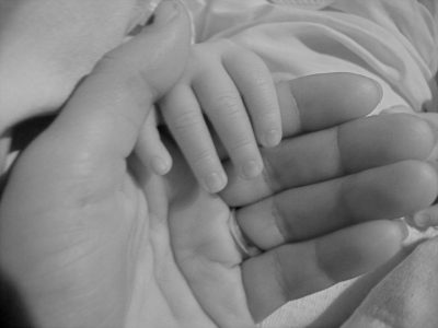 A greyscale image of a mother's hand touching her child's