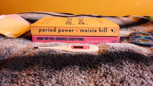 An image of two books that are mentioned throughout the article, stacked upon one another, with a thermometer, and condoms and sanitary towels next to the books.