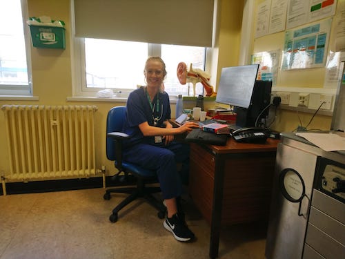 Dr Elen Pigott seen in her scrubs sat at her desk