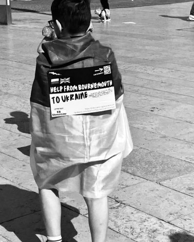 The back of a young boy with a Ukrainian flag wrapped round him and a small placard hung on his back reading, 'Help from Bournemouth to Ukraine'