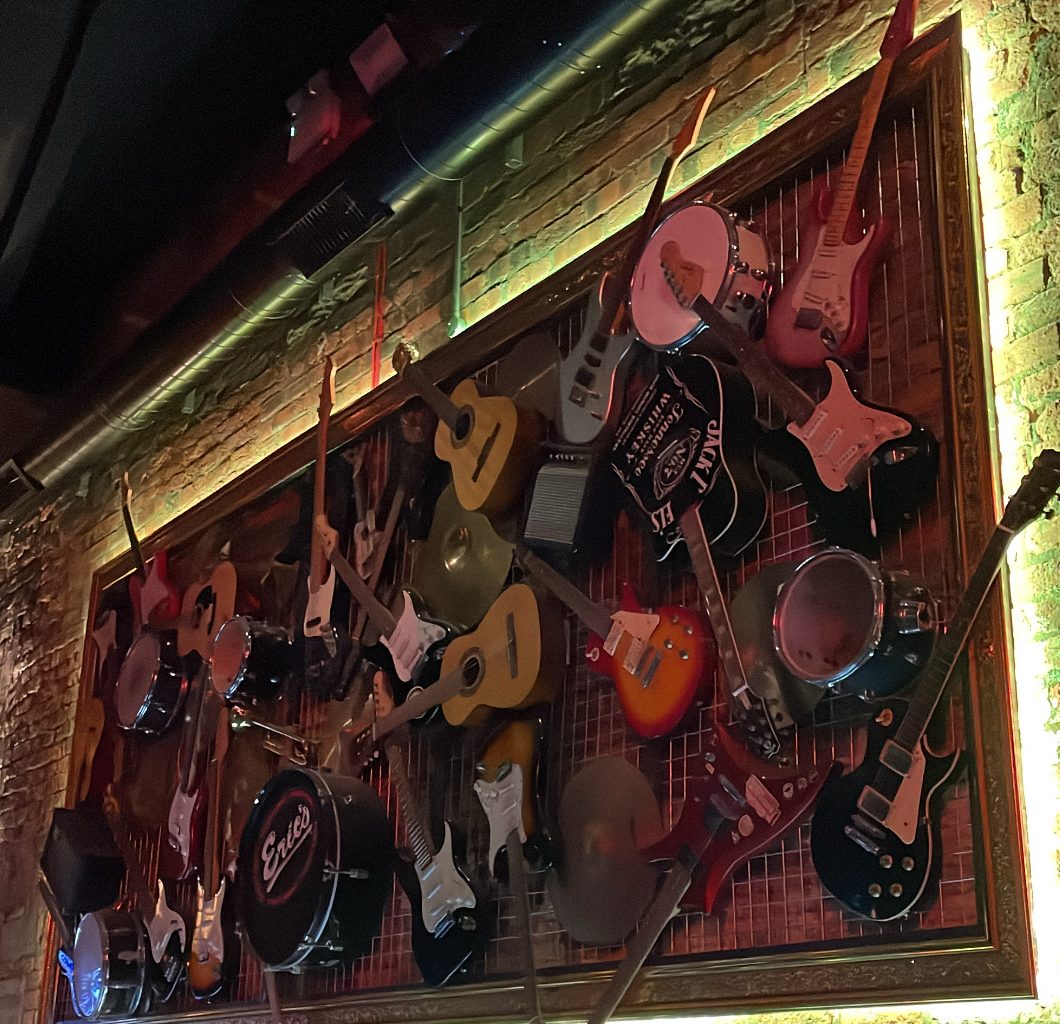 Photo of lots of different types and brands of guitars hung on the wall.