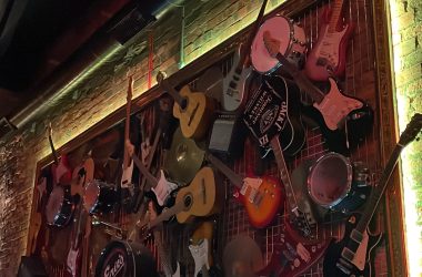 Photo of lots of different types and brands of guitars hung on the wall.